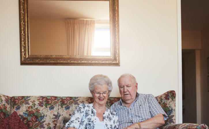 Portrait of happy old couple sitting together at home on sofa and using digital tablet. Elderly man and woman using touchscreen computer at old age home.