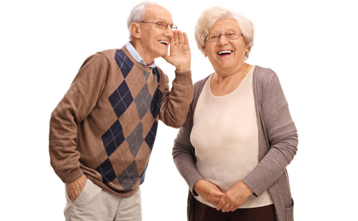 Studio shot of an old man whispering something to his wife isolated on white background