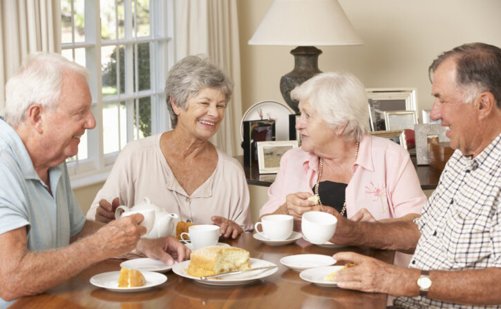 Group Of Senior Couples Enjoying Afternoon Tea Together At Home Laughing Amongst Themselves