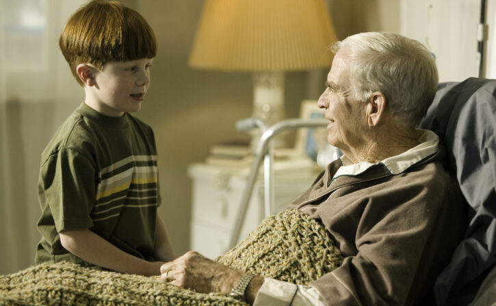 Grandson (8-9) talking to grandfather in bed in retirement home