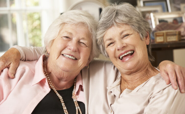 Portrait Of Two Retired Senior Female Friends Sitting On Sofa Smiling And Laughing with Each Other.